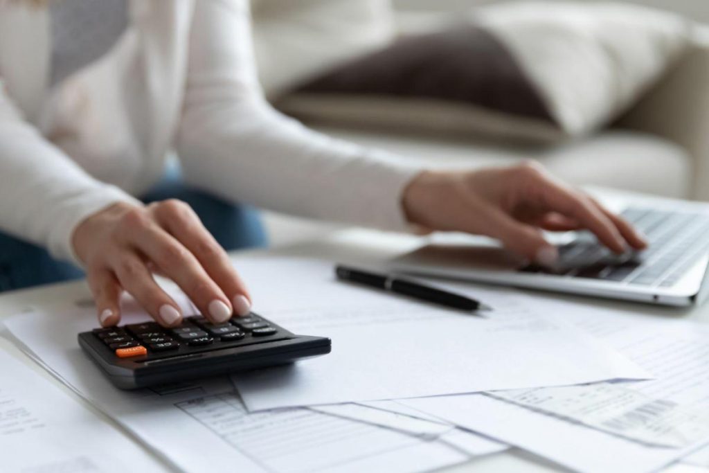 Close-up de mulher calculando impostos de importação no laptop e calculadora